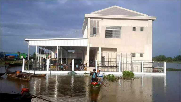 The white Le Van Khanh school building with floodwater all around and a student in a boat in front
