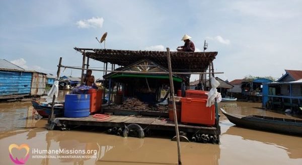 A floating fish-processing boat home on Tonle Sap Lake, with blue and red coolers under a thatch roof