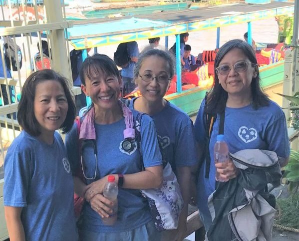Four women on the IHM medical team wearing matching blue IHM t-shirts, smiling on the boat to the floating villages