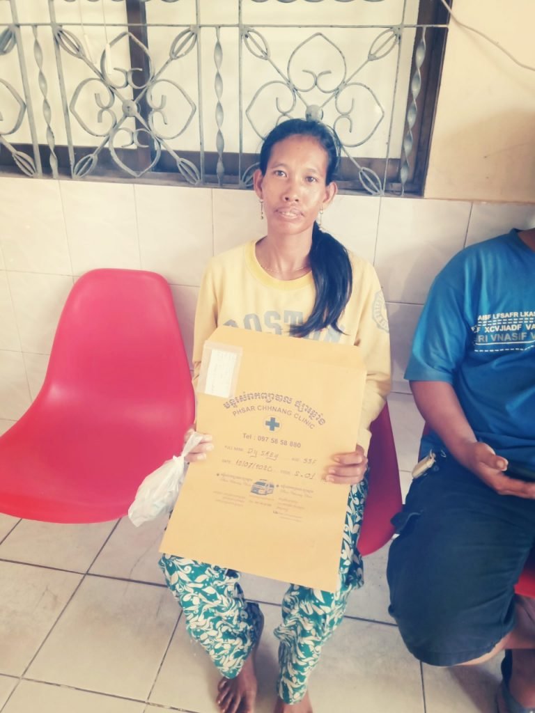 A woman in a yellow sweater holding her medical care package envelope from the Phsar Chhnang Clinic, made possible by IHM donor support