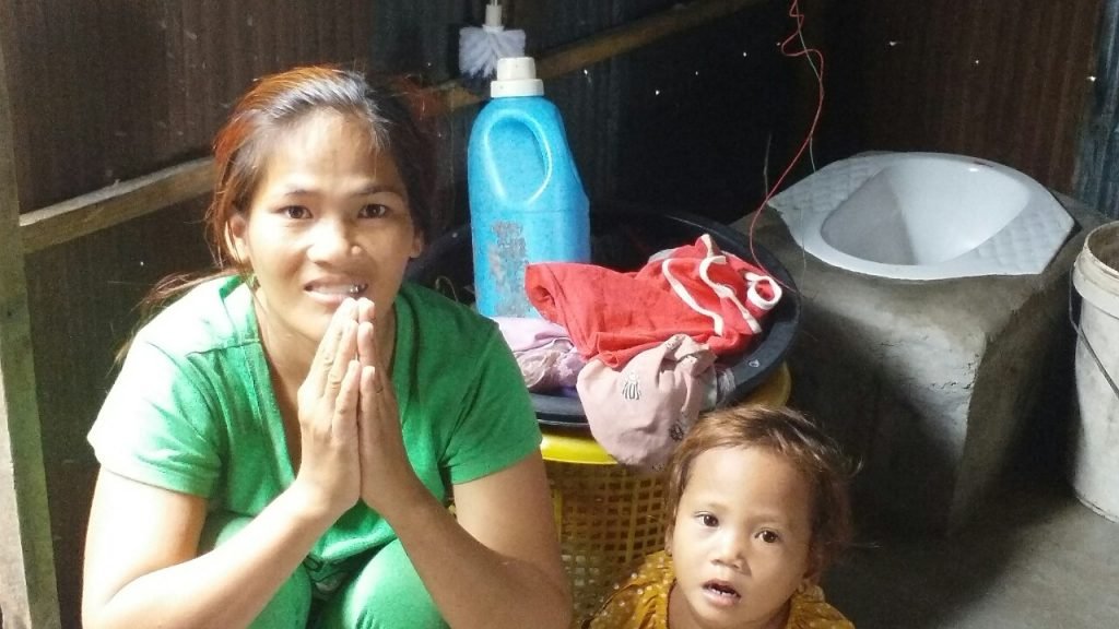 A mother in an orange shirt holding her young child outside the Phsar Chhnang Clinic, where the family received medical care for the first time