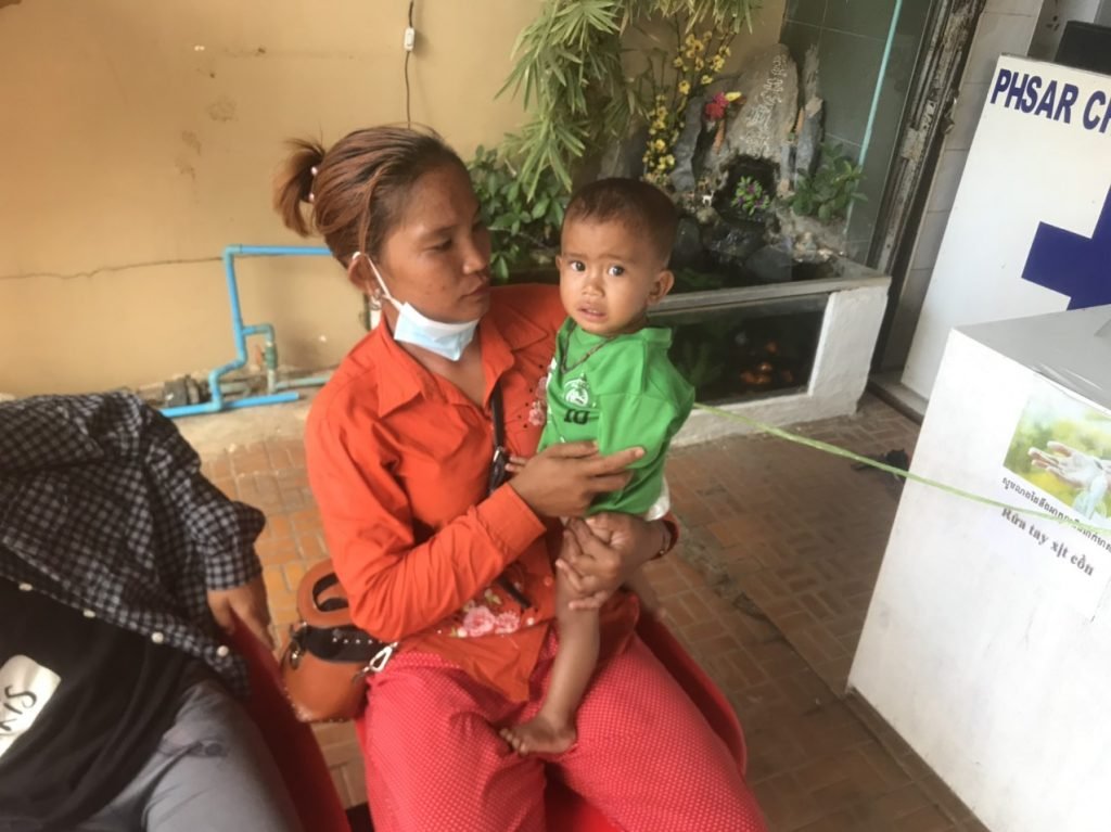 A young mother in a green shirt with her toddler beside the new portable toilet that IHM provided for their home