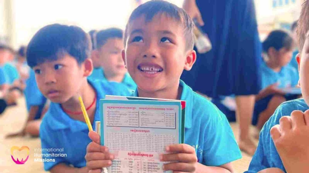 A young Le Van Khanh student smiling broadly as he holds up his Khmer-language workbook